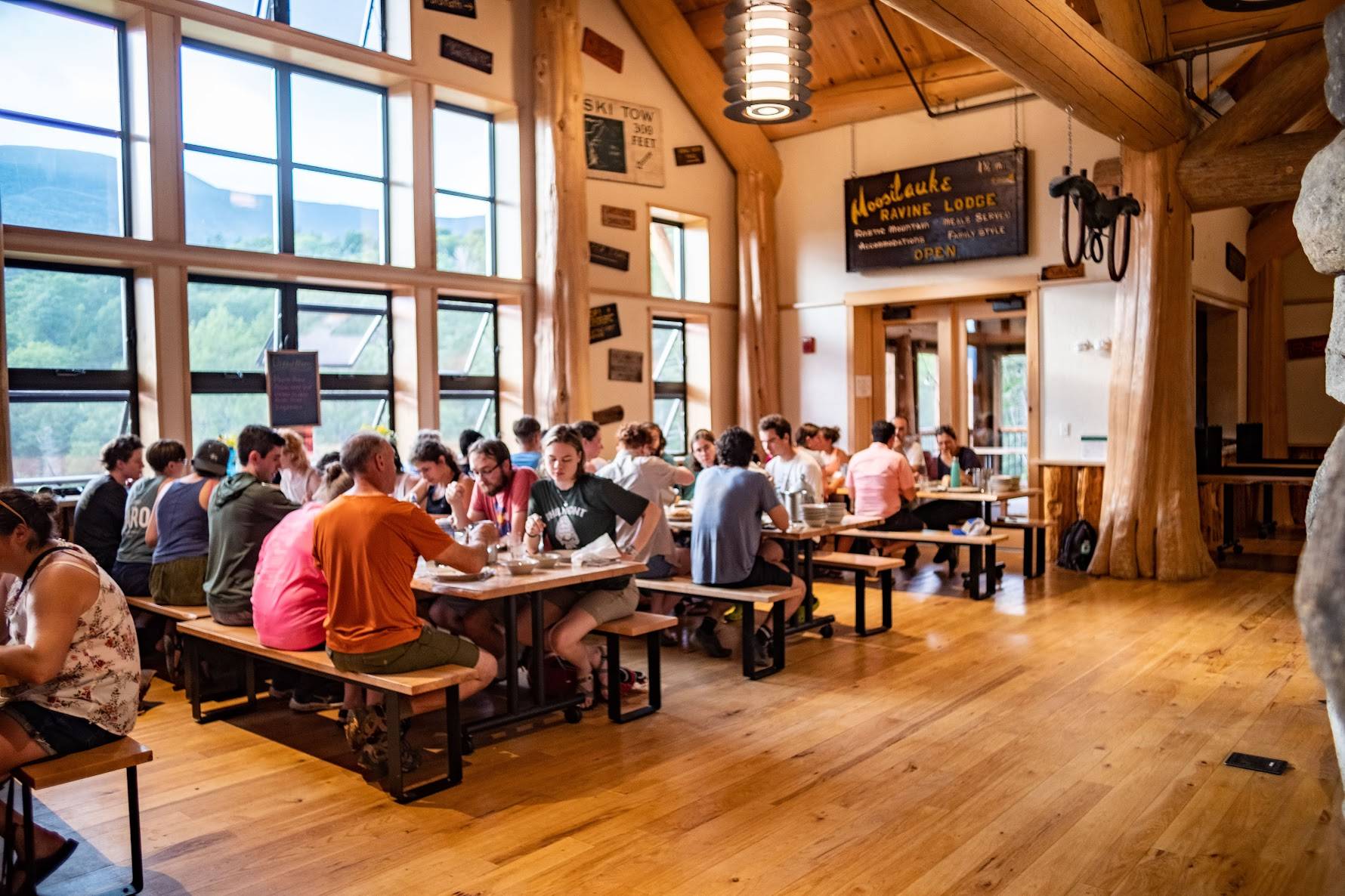 About 25 students and community members sit at tables in the main room of the Lodge during dinner service. 